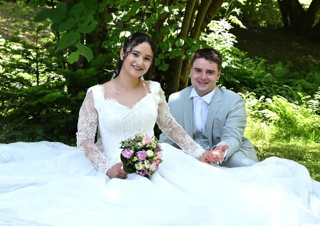 Brautpaar sitzt lachend auf der Wiese, das Brautkleid weit ausgebreitet