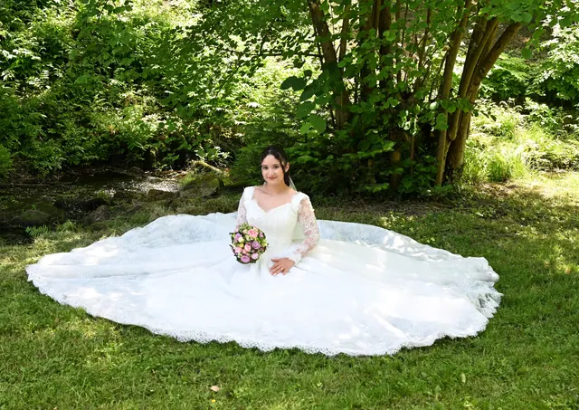 Braut sitzt im ausgebreiteten Brautkleid auf der Wiese